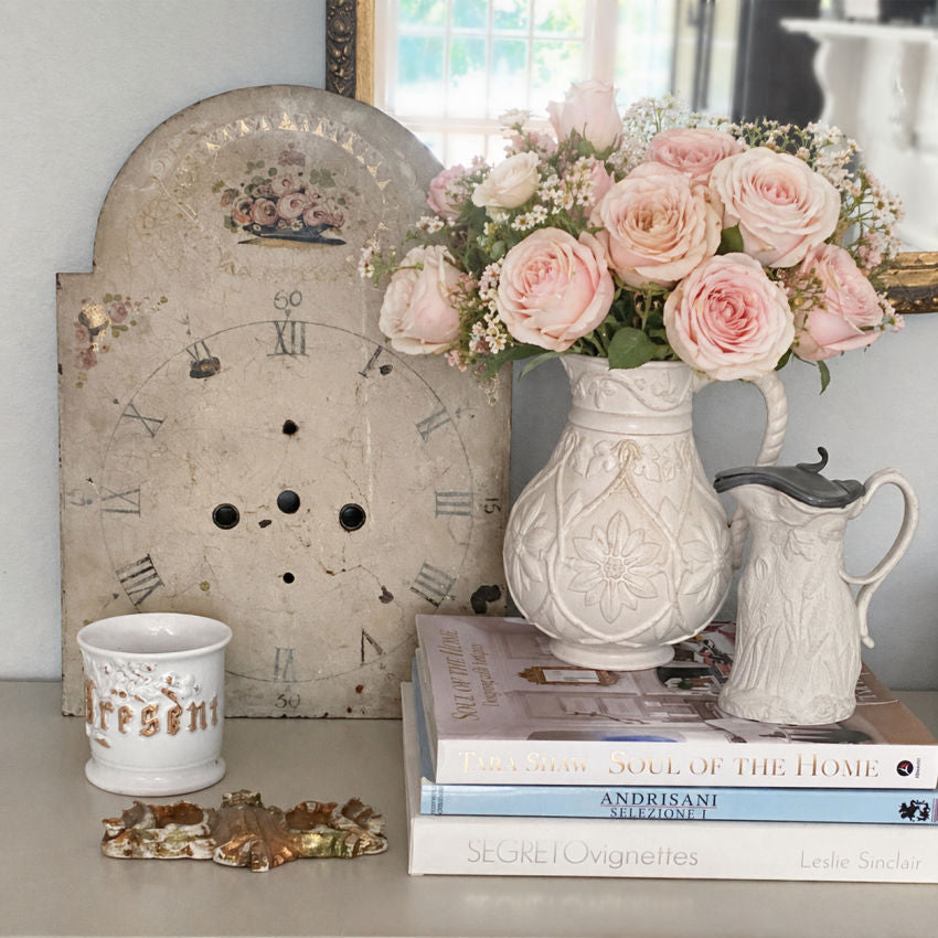 large antique clock dial styled with gilt antique cup,, drabware pitchers and pink roses in front of antique gilt mirror