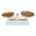 An antique French balance scale with white and aqua blue painted details and two brass weighing trays.