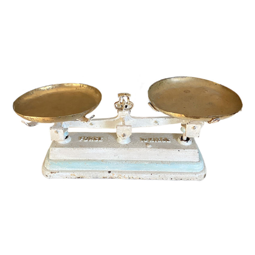 An antique French balance scale with white and aqua blue painted details and two brass weighing trays.
