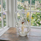 Antique Mary Gregory glass pitcher with hand painted boy and white enamel trees in garden room with view outside of flowers