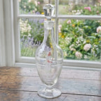 Antique Mary Gregory glass decanter with white enamel figure styled on an antique French cabinet in a country home