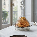 Antique silver-plated champagne bottle coaster on a French table with white linen and Paris view holding a crystal decanter
