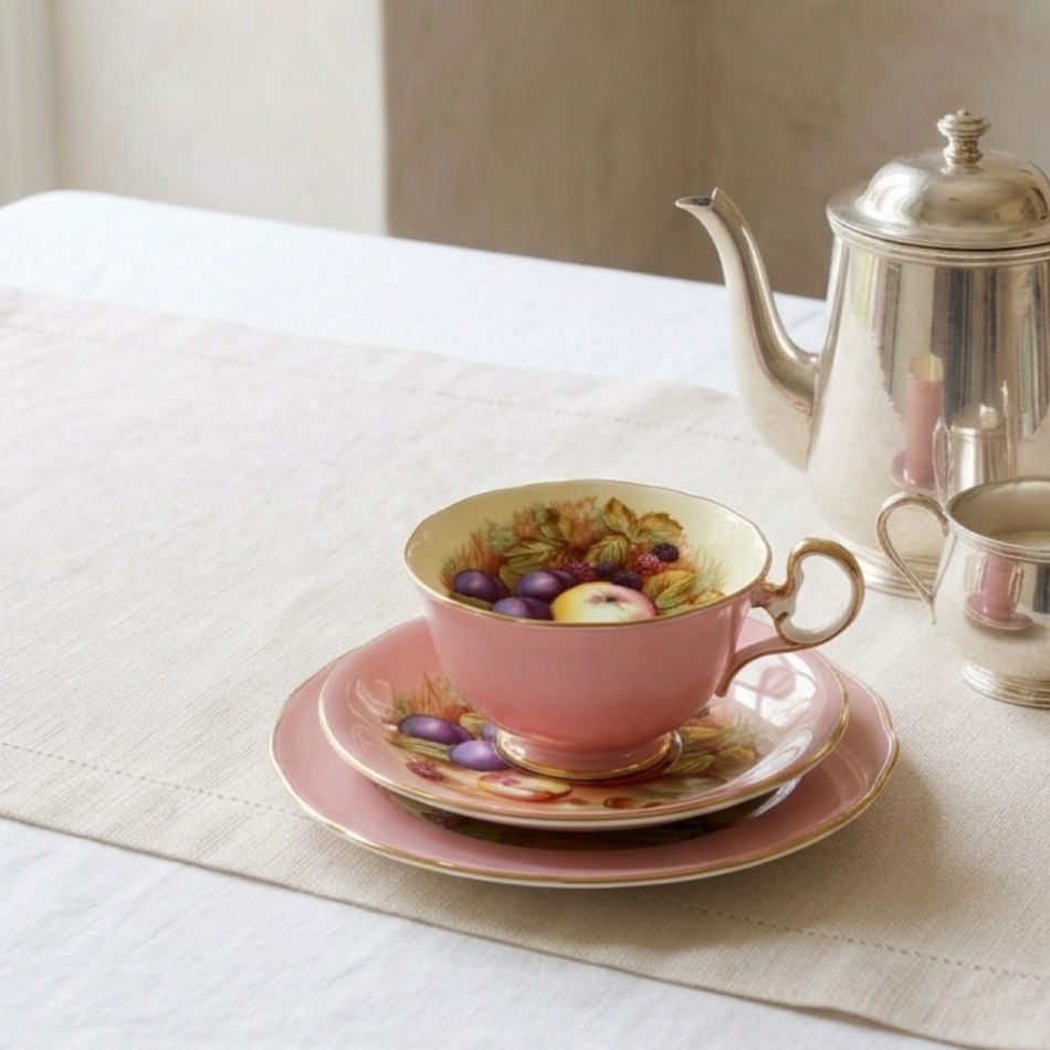 Pink English bone china tea trio styled on white linen with silver tea service