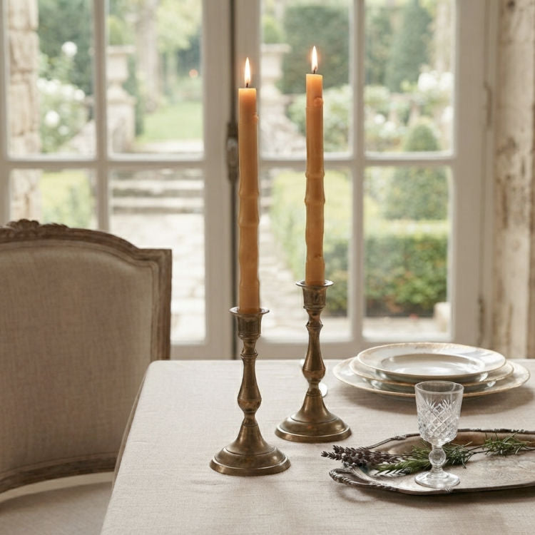 Natural bamboo beeswax taper candles displayed in antique brass candlesticks on an elegant French country table