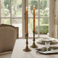 Natural bamboo beeswax taper candles displayed in antique brass candlesticks on an elegant French country table