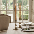 Natural bamboo beeswax taper candles displayed in antique brass candlesticks on an elegant French country table