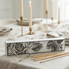 Black and white Art Nouveau matchbox with long wooden matches beside a candle