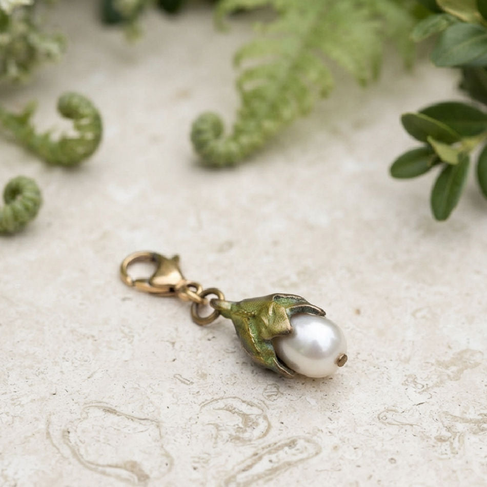 Michael Michaud cast bronze Leaf charm with freshwater pearl on French limestone in a garden setting