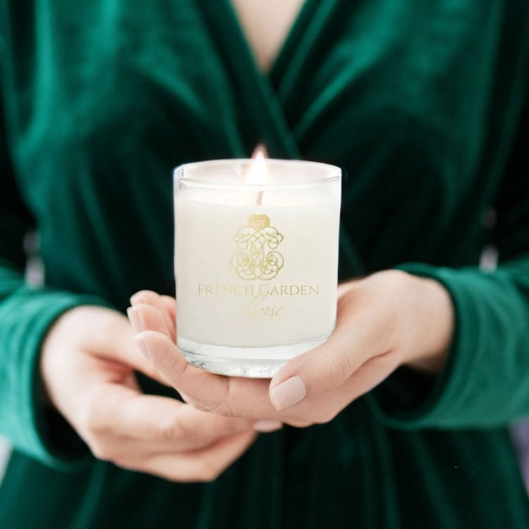 Woman in green velvet holding a glowing luxury scented candle in an elegant French-inspired interior
