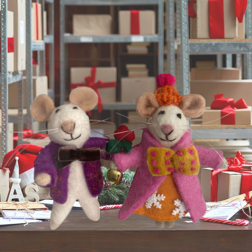 Two toy mice in colorful clothing holding hands with gift boxes and decorations in the background.