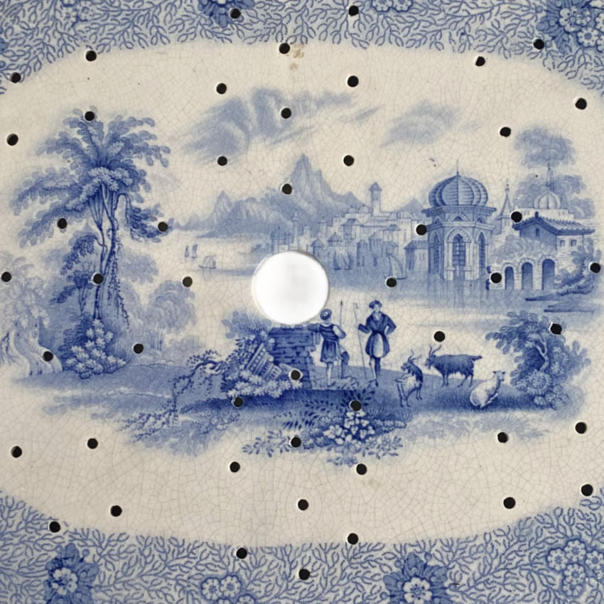 Early English ceramic strainer drainer, top‑down view showing shepherds and river scene pattern