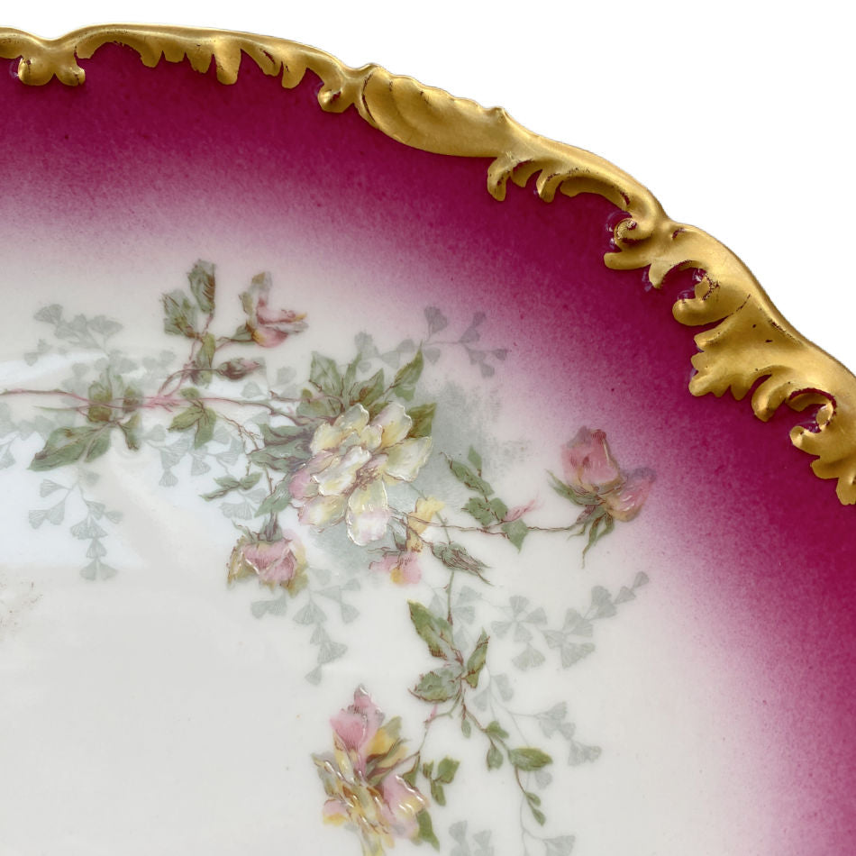 close up of Early 1900s T&V Limoges porcelain plate with pink and yellow roses, cerise pink border, and elaborate gilt scalloped rim.
