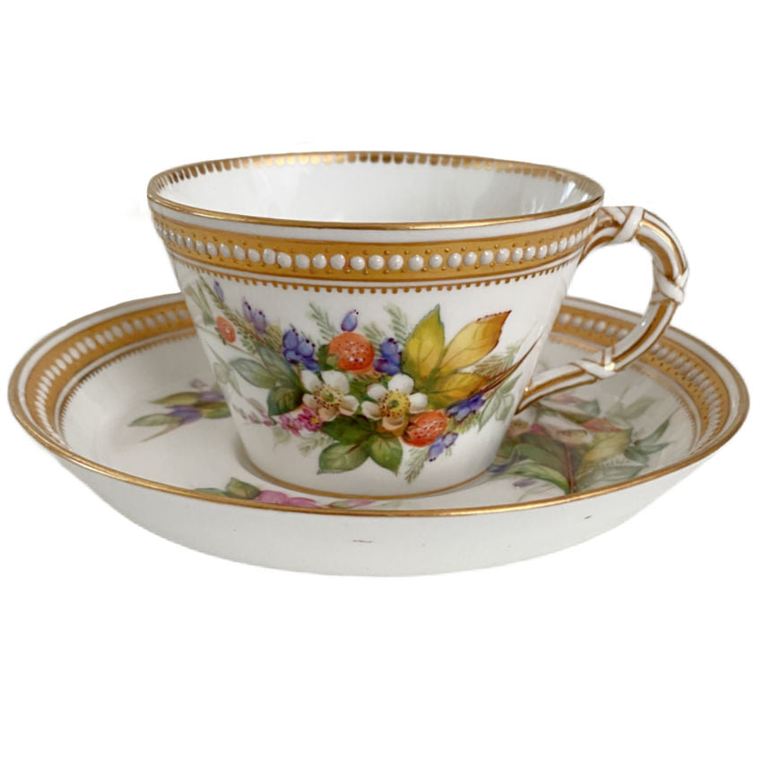 Detail of an antique Royal Worcester cup with its own floral painting, delicate gilding, and raised jeweled ornament