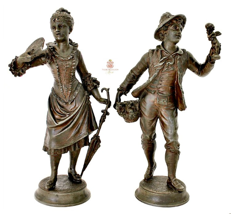 A pair of antique French bronze sculptures, depicting a peddler and a young woman with a fan, placed on separate bases.