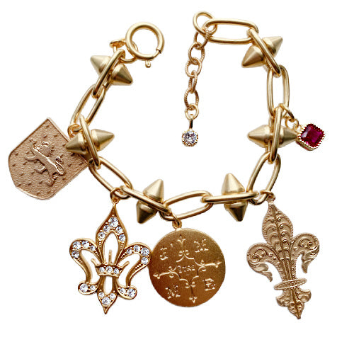 gold French heritage bracelet with fleur-de-lis, lion shield, crystal accents, and reproduction coin, small ruby dangle. Parisian artisan design with timeless elegance.