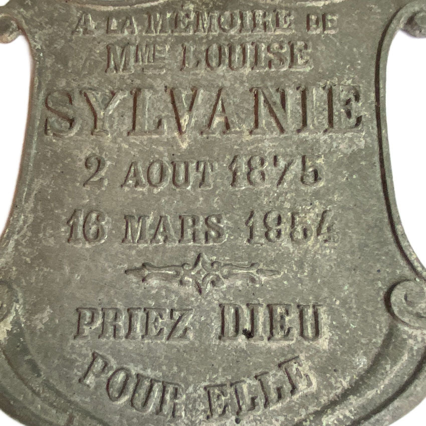 Close-up of raised lettering on French cemetery memorial plaque, showing grey cast metal patina and historic wear