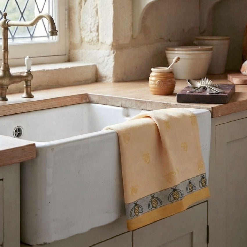 Antique French kitchen sink with woven bee jacquard towel draped naturally over the sink, French country kitchen, natural light