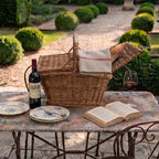 French hand woven willow  picnic basket styled in a French garden on antique table with wine, plates, and antique French linen