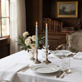 Heirloom Ocean hand dipped taper candles glowing in antique silver candlesticks on an elegant dining table