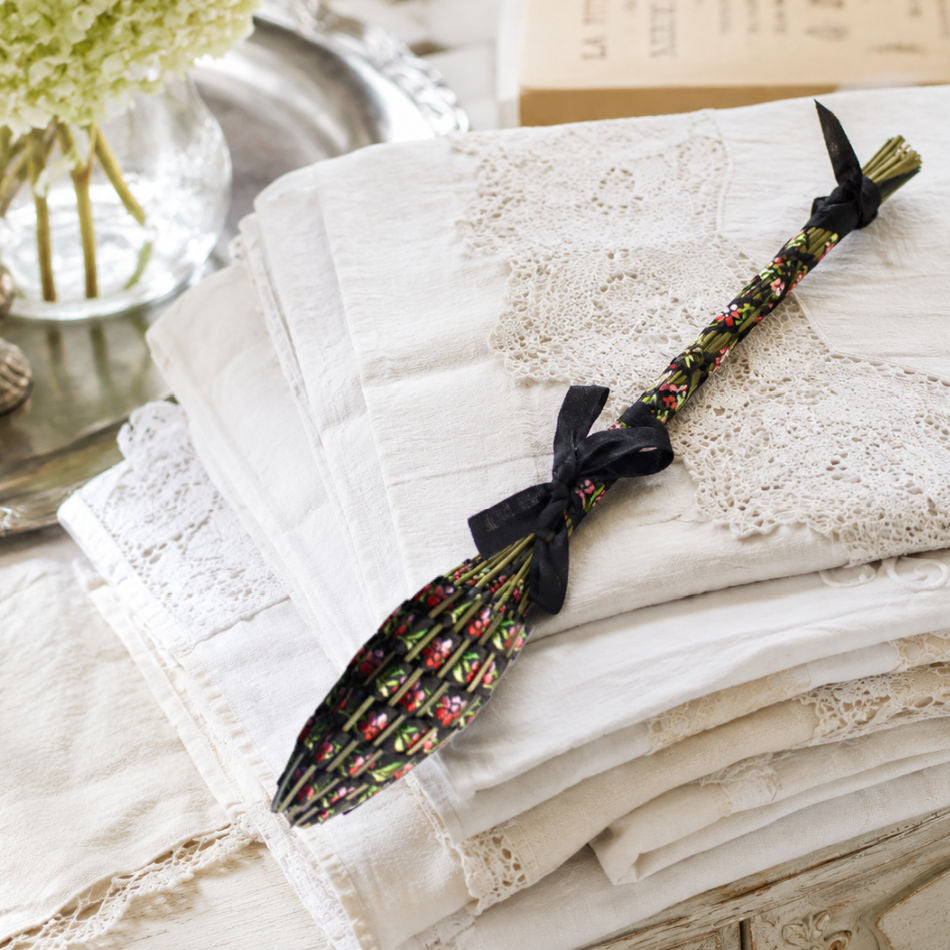 Hand woven French lavender Fuseau de Lavande wand black brocade on stack of antique linens