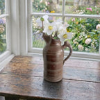 antique french wine pitcher filled with helleborus flowers in french country sunroom
