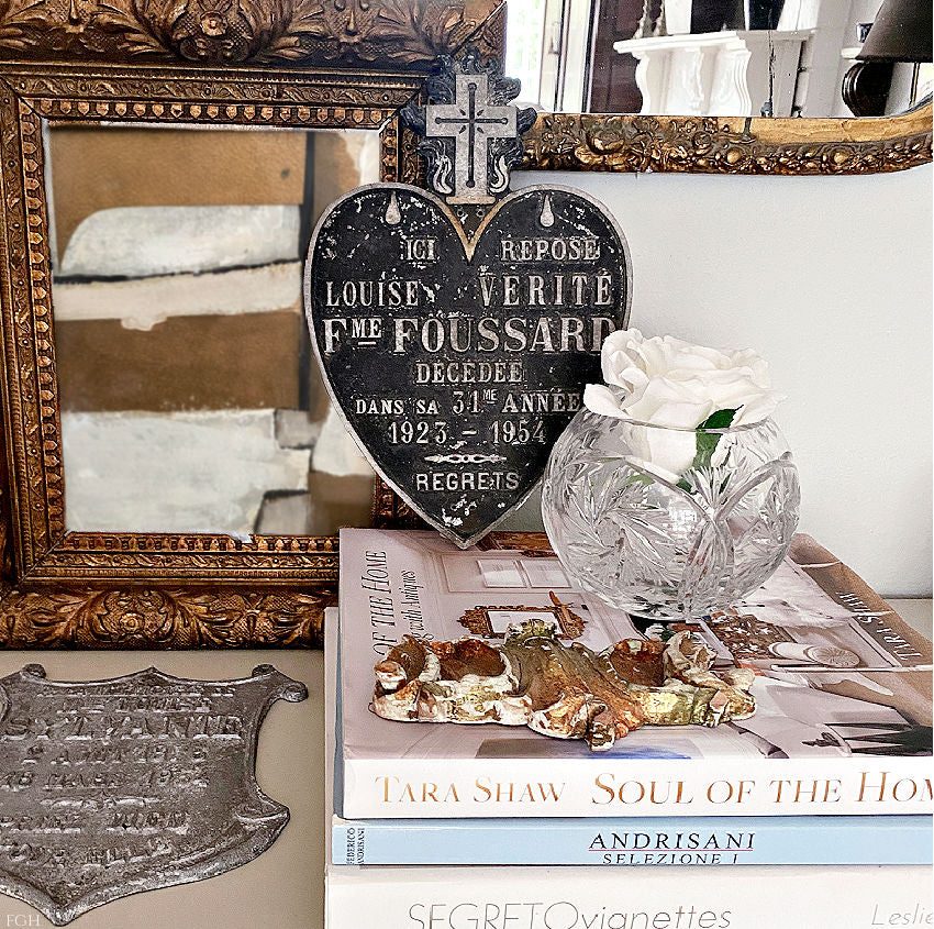 Display of mid-century French Sacred Heart plaque among antiques, with modern art in gold frame and rose and decorator books