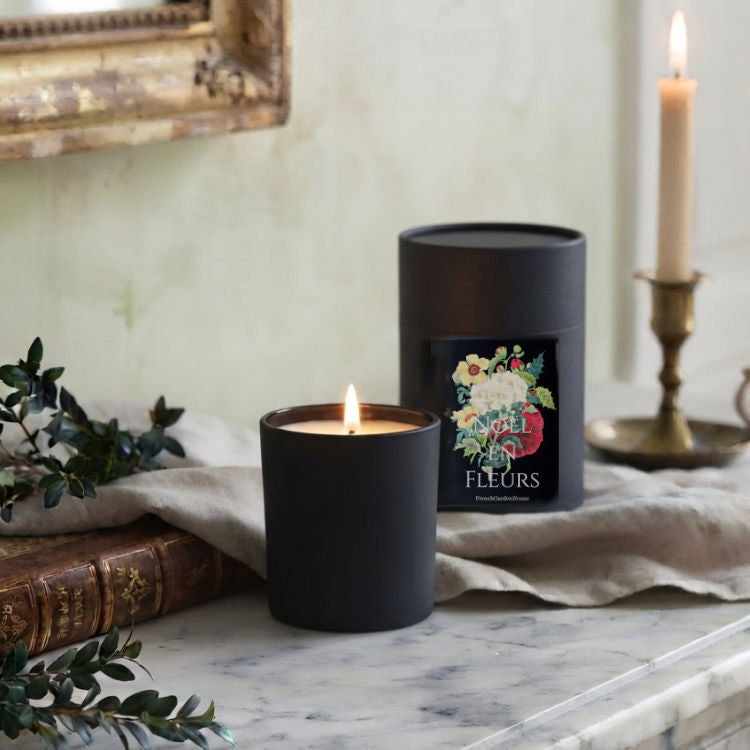 Noël en Fleurs luxury candle with FrenchGardenHouse gift box displayed on a marble mantel with French book and boxwood greenery