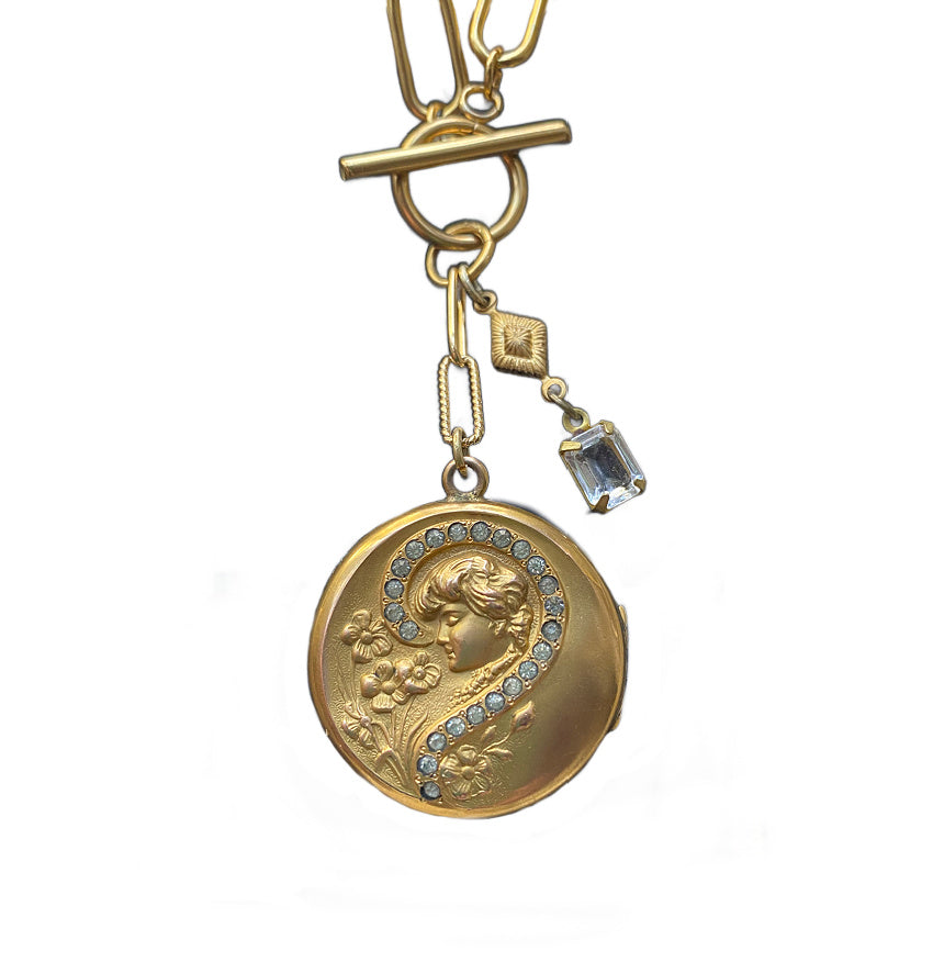 Antique Art Nouveau gold locket charm necklace with a repousse design of a lady and flowers, featuring a paste diamond question mark, on a gold-plated chain.