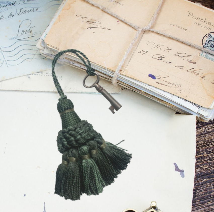 Small green French tassel with antique desk key, charming woven threads and authentic patina—an elegant decorative accent for French country styling.