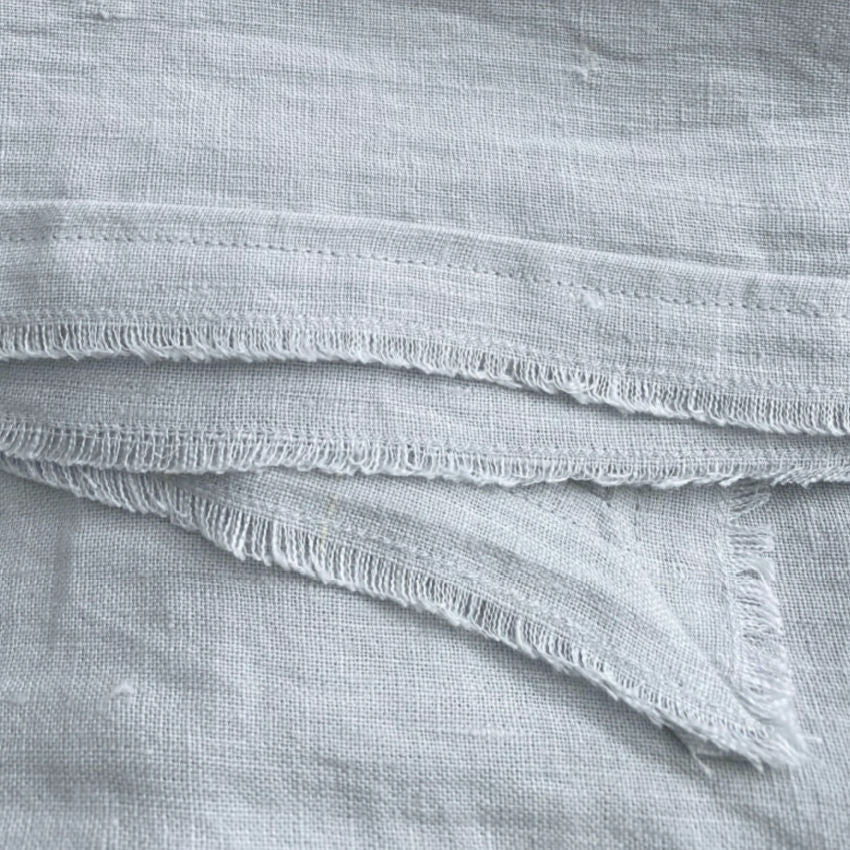 Close view of ocean blue-green linen fabric texture showing soft weave and gently frayed edge
