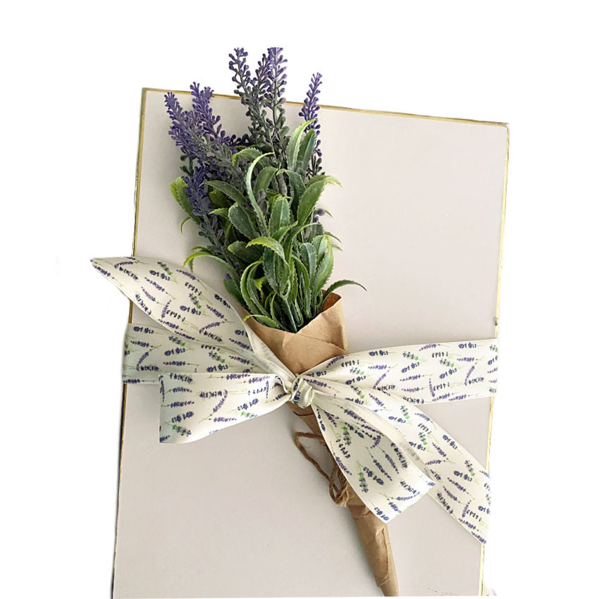 Gift box tied with satin white ribbon with lavender flowers on it, tied with a bundle of French dried lavender.
