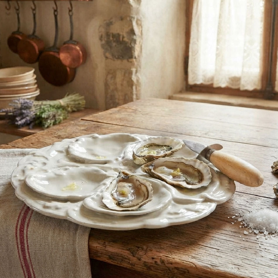Antique French Limogs Oyster Plate in blanc de chine on a table with oysters, a shuckiing knife and french linen.