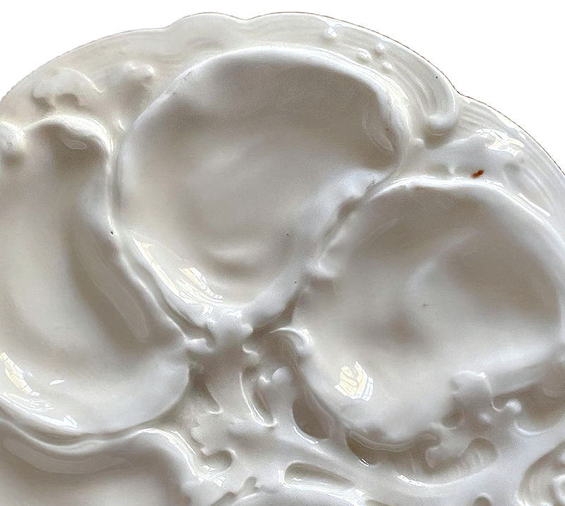 A white porcelain 19th Century French Limoges oyster plate with leafy seaweed design around the shell-shaped wells.