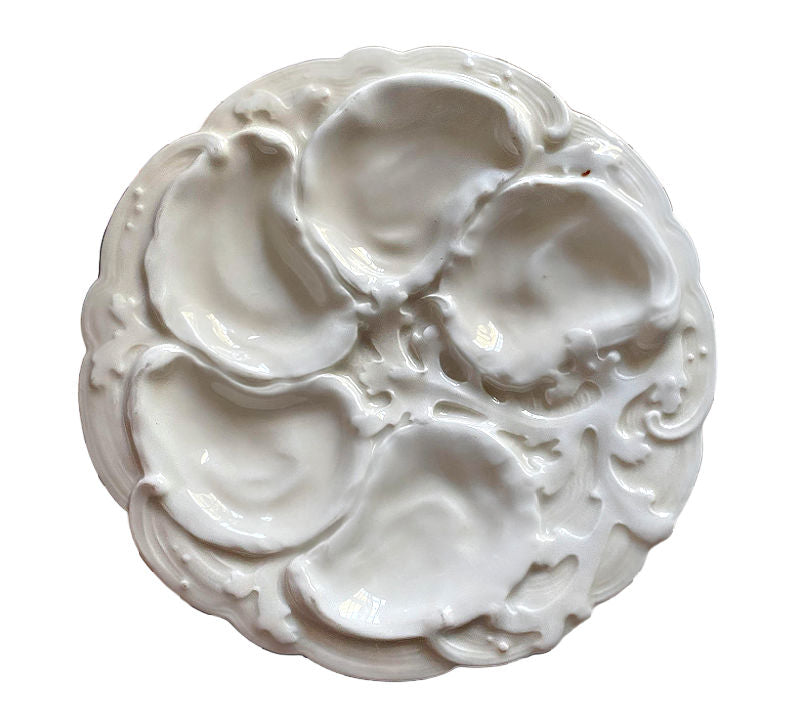 A white porcelain 19th Century French Limoges oyster plate with leafy seaweed design around the shell-shaped wells.