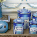 Set of antique French blue striped enameled canisters with labels on a wooden surface