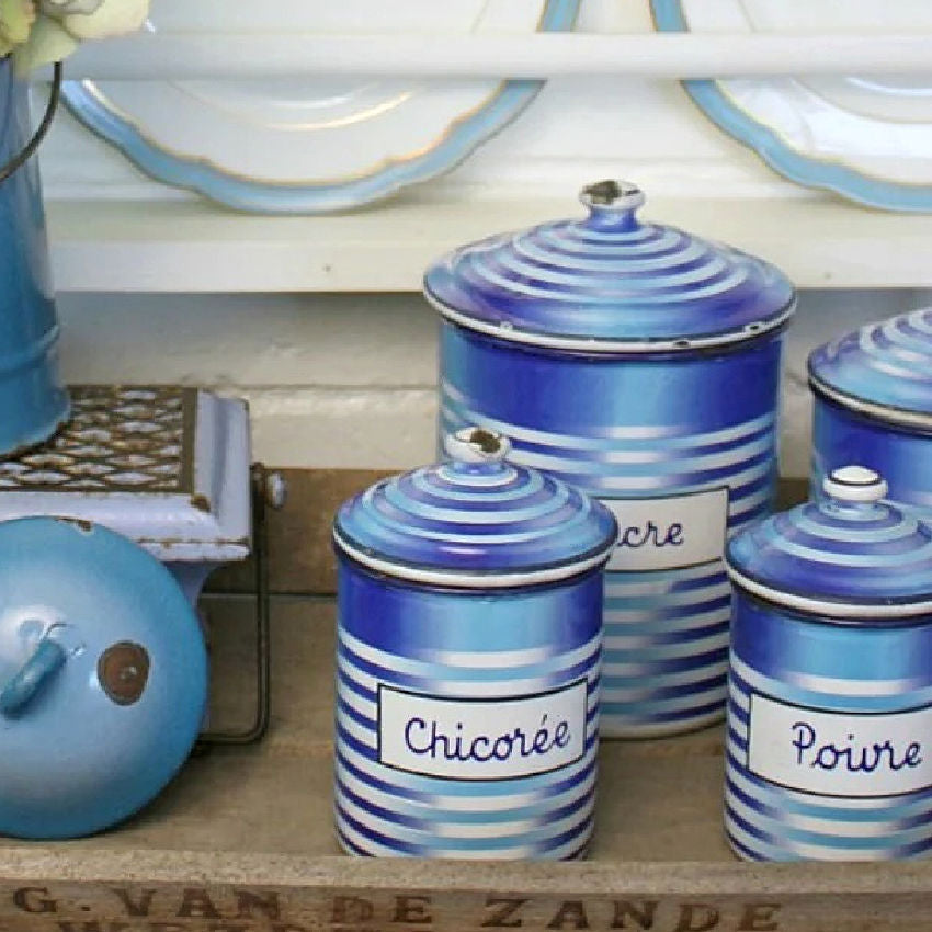 Set of antique French blue striped enameled canisters with labels on a wooden surface