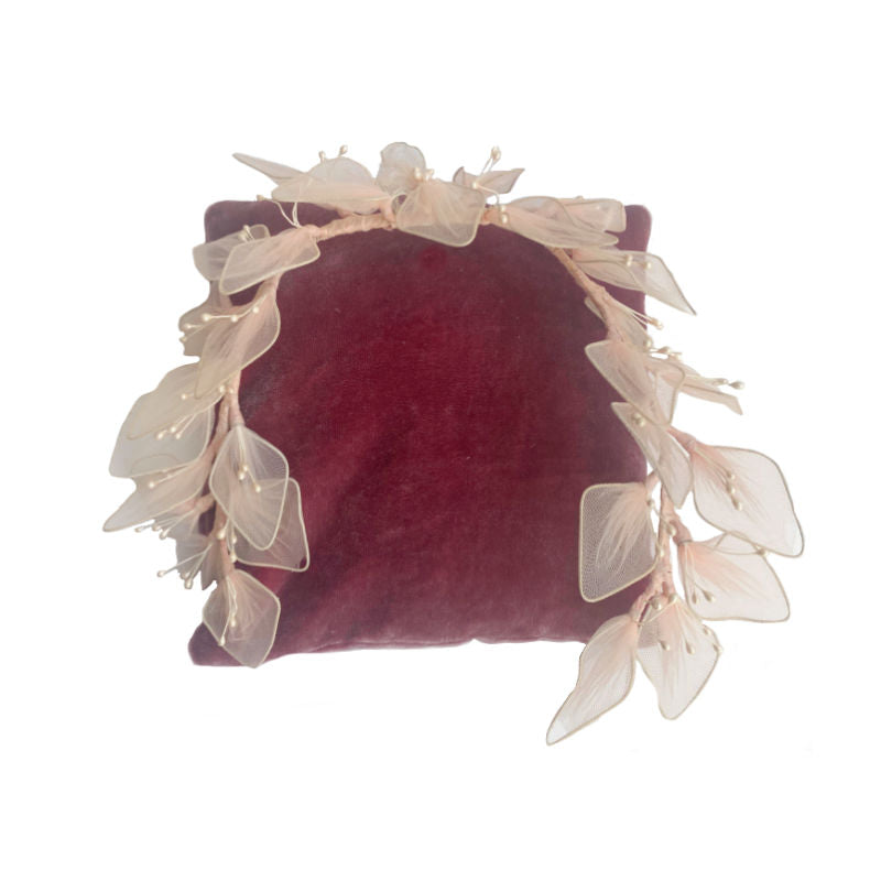 A vintage pink floral head crown with white flowers and pearlized stamens, displayed on a red velvet surface.