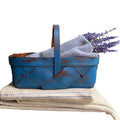 Hand-woven wood splint basket with authentic French blue patina, styled on a stack of antique French towels in blue and cream with lavender.