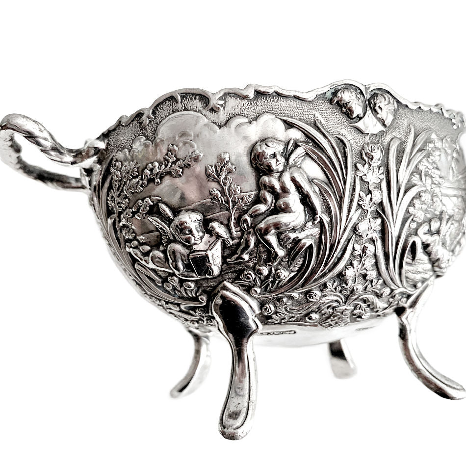 Close-up of cherubs reading a book and floral relief on vintage silver plated bowl