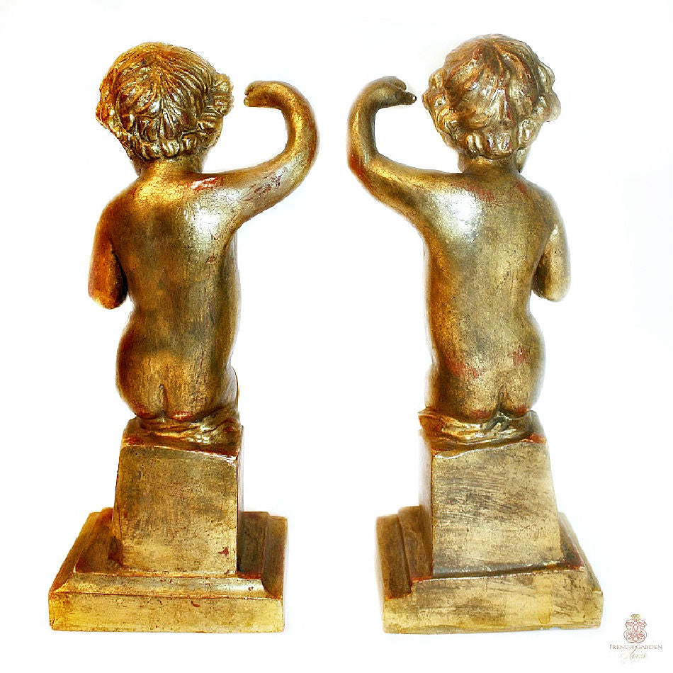 A pair of antique hand-carved gilt wood putti or cherubs standing on square bases, with gold leaf finish and showing signs of age-related wear.