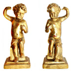 A pair of antique hand-carved gilt wood putti or cherubs standing on square bases, with gold leaf finish and showing signs of age-related wear.