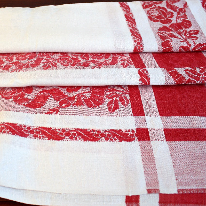 Close view of antique French red and white damask tablecloth highlighting intricate rose motif and bourdon embroidered monograms
