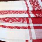 Close view of antique French red and white damask tablecloth highlighting intricate rose motif and bourdon embroidered monograms