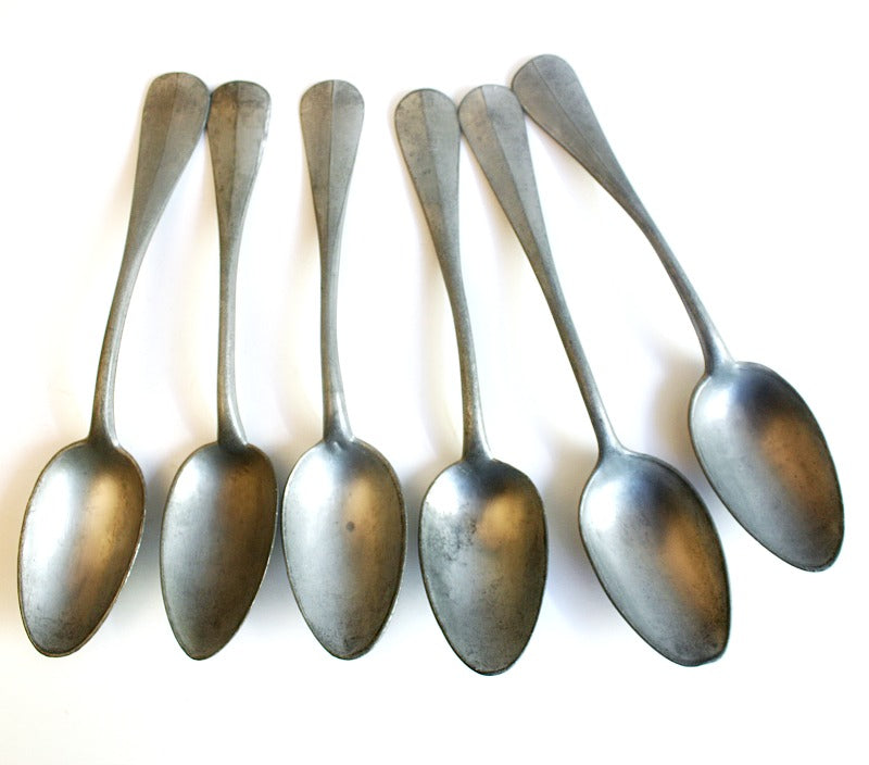 A set of six silver pewter spoons displayed in a French Country rustic antique oak wood rack.