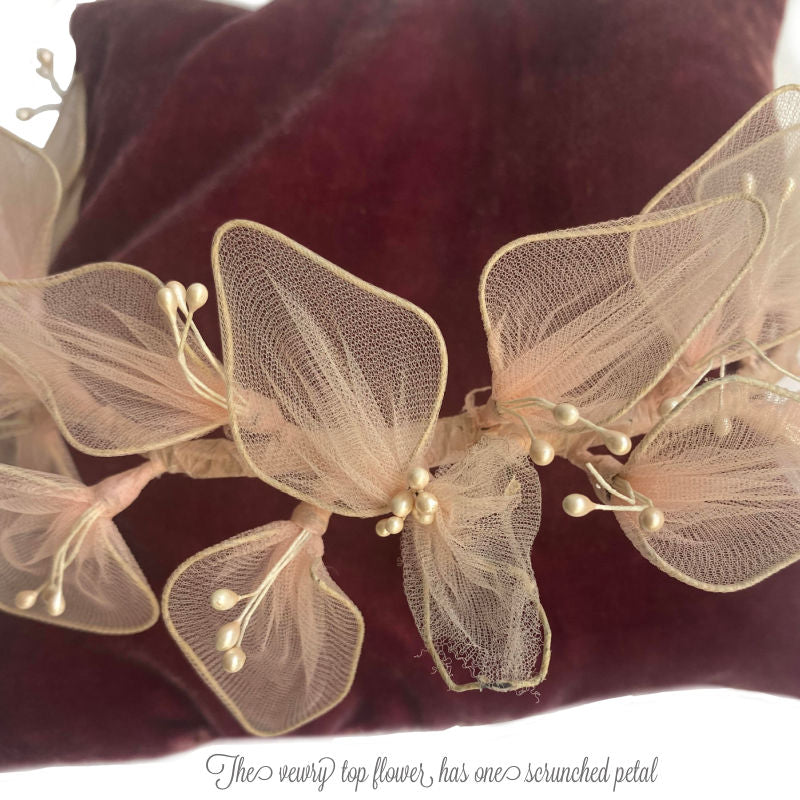 A vintage pink floral head crown with white flowers and pearlized stamens, displayed on a red velvet surface.