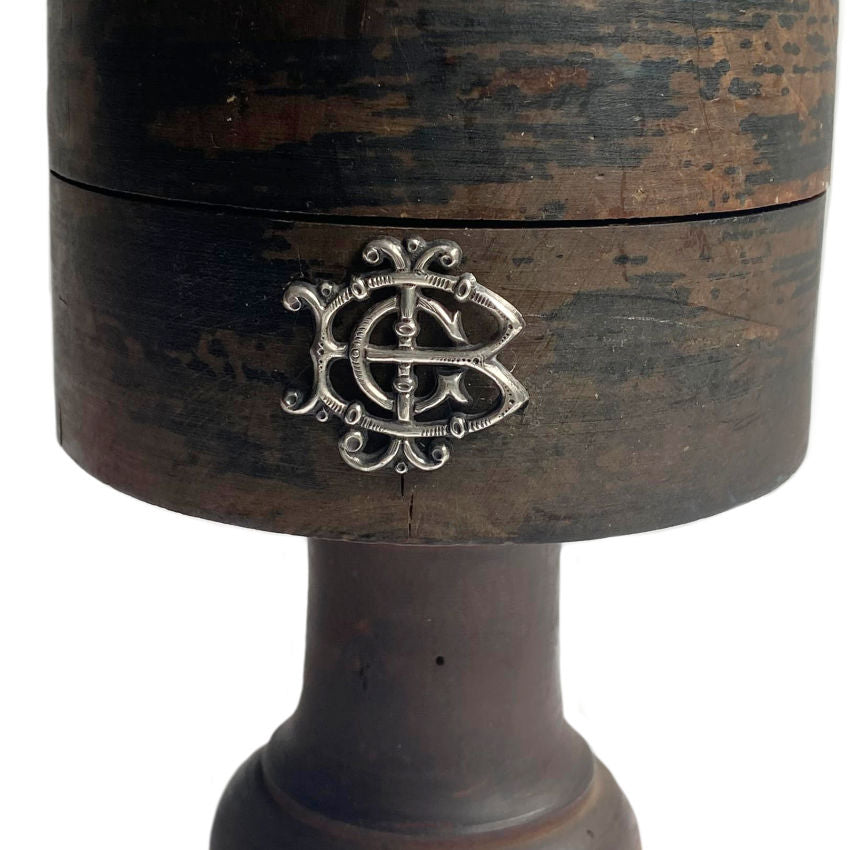 Antique French wooden hat block stand with a silver monogram on the front, displaying signs of aging and use.