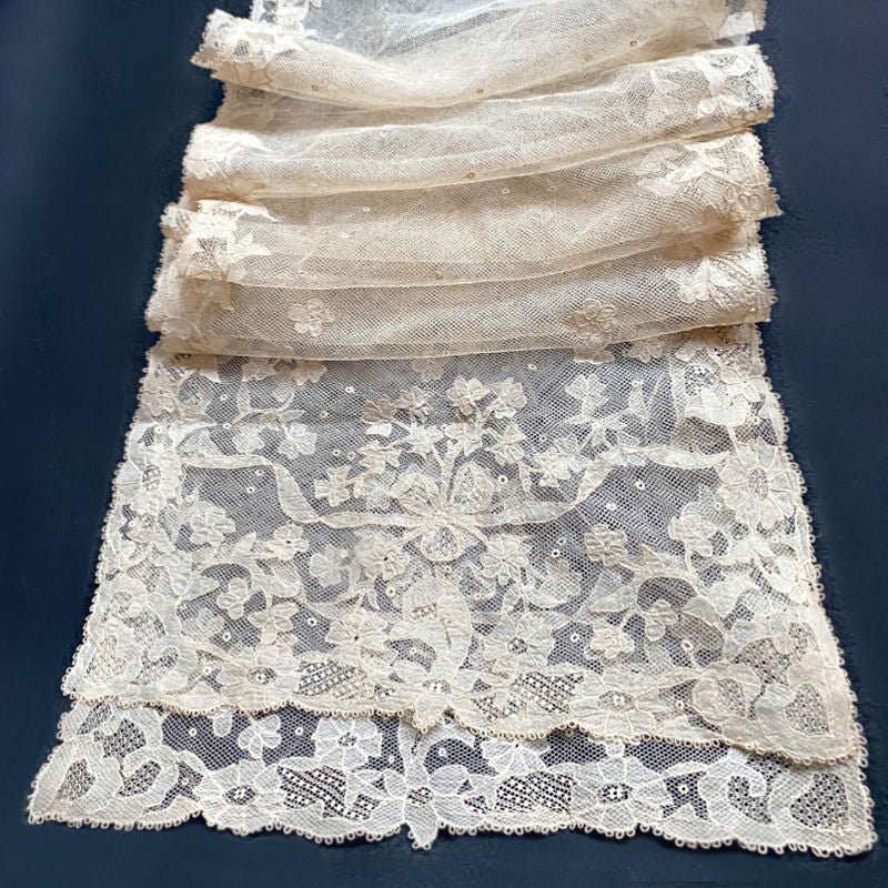 A antique hand made Brussels lace bonnet veil with floral patterns and ribbon bows, predominantly in a beige or light cafe au lait color.