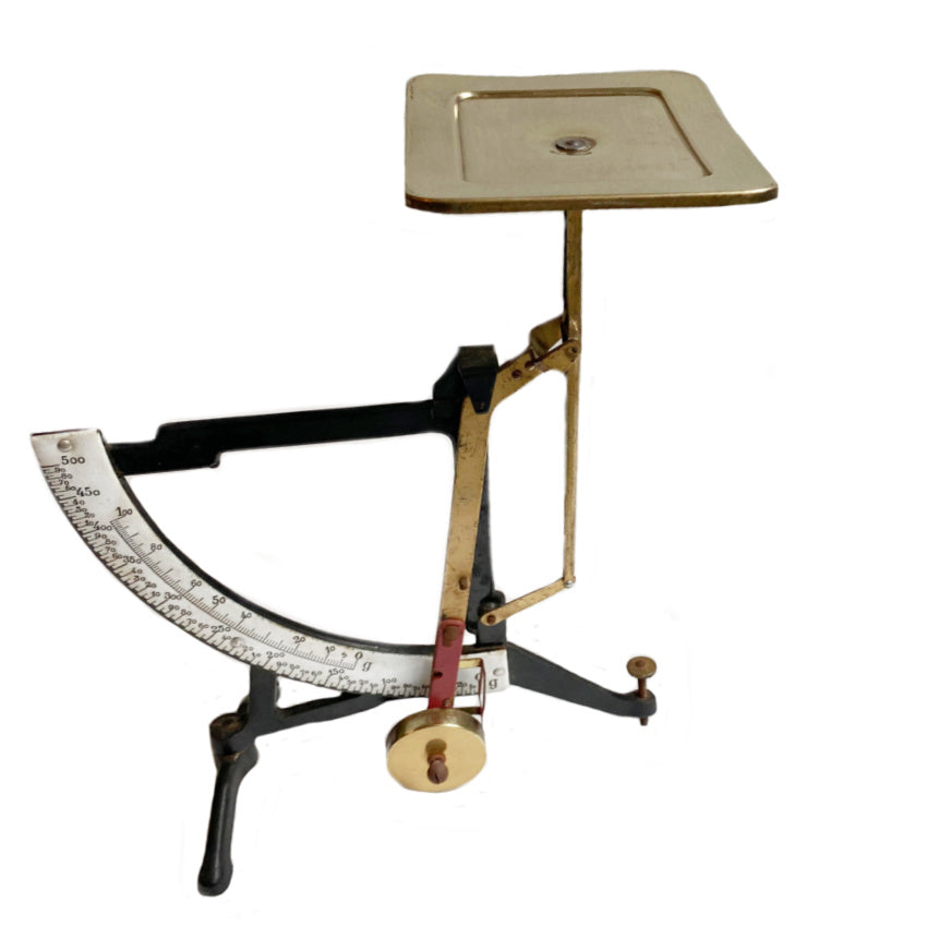 Antique European enameled postal scale with brass, featuring a black iron base, white enamel scale, and brass weighing platform.