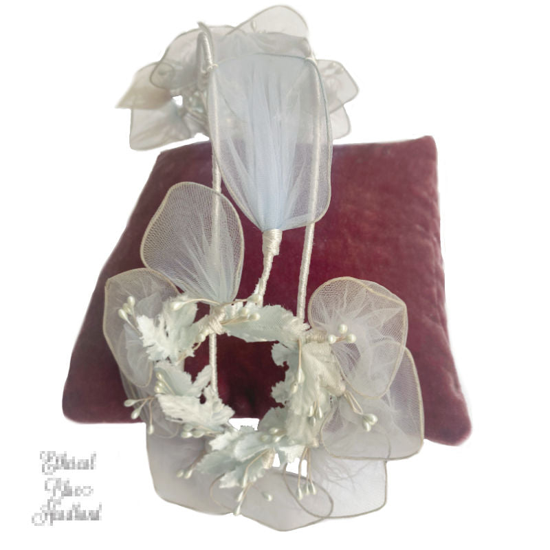 A vintage ethereal blue floral head crown with pearlized stamens and satin leaves, displayed on a red cushion.