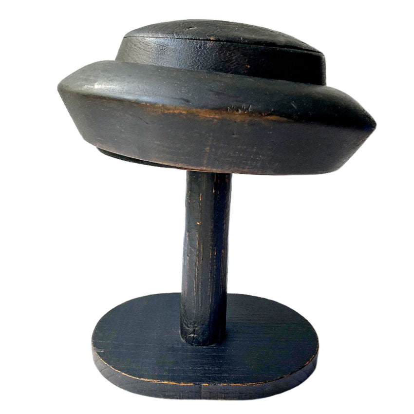 A French 19th Century millinery shop wood hat block stand with a dark patina, featuring a rounded hat form sitting atop a three-piece stand.